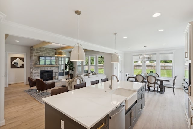 kitchen with light wood-type flooring, a stone fireplace, decorative light fixtures, and a center island with sink