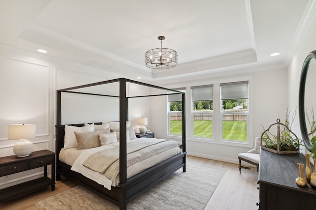 bedroom featuring light wood-type flooring, an inviting chandelier, crown molding, and a tray ceiling