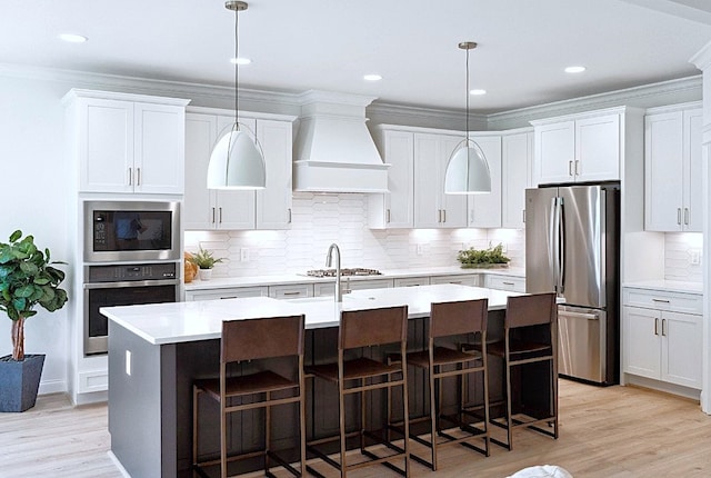 kitchen with premium range hood, hanging light fixtures, stainless steel appliances, an island with sink, and white cabinets