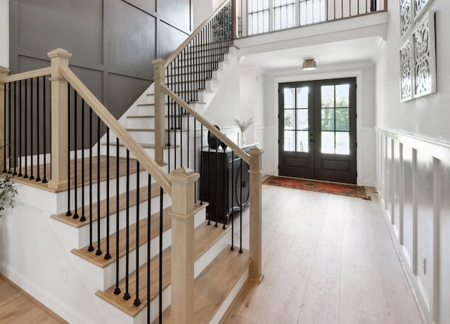 entrance foyer with french doors, a decorative wall, a high ceiling, ornamental molding, and hardwood / wood-style floors