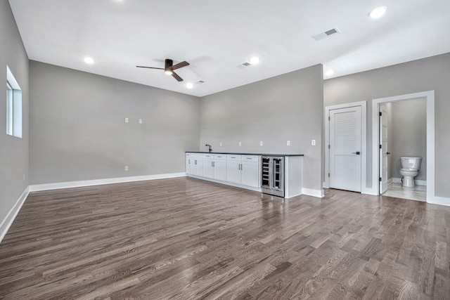 unfurnished living room with sink, ceiling fan, beverage cooler, and dark hardwood / wood-style flooring