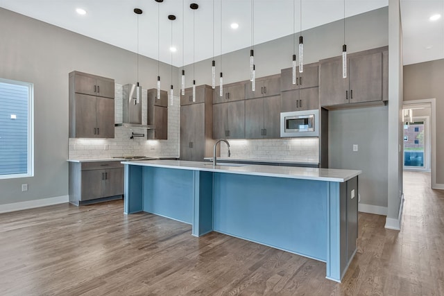 kitchen with stainless steel microwave, decorative light fixtures, an island with sink, and sink