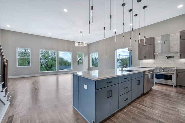 kitchen with a kitchen island with sink, wall chimney exhaust hood, sink, decorative light fixtures, and appliances with stainless steel finishes