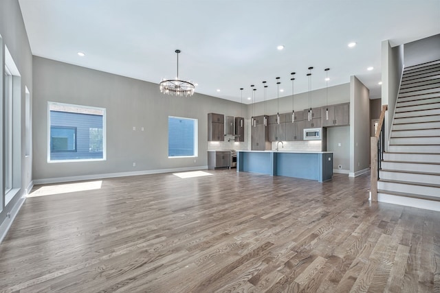 unfurnished living room featuring an inviting chandelier, light hardwood / wood-style flooring, and sink