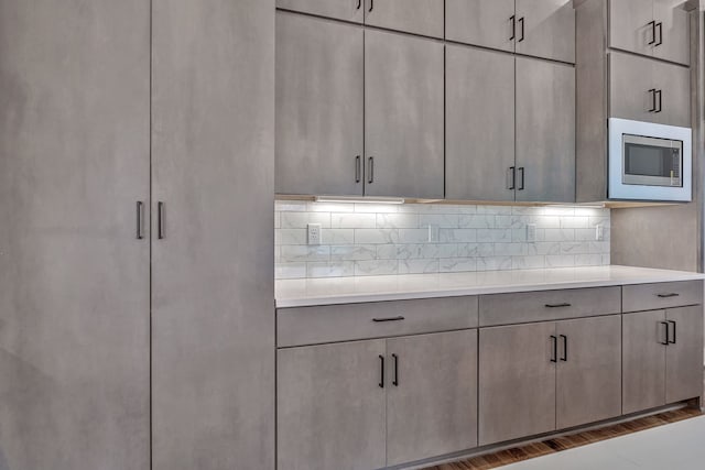 kitchen featuring stainless steel microwave, decorative backsplash, dark wood-type flooring, and gray cabinetry