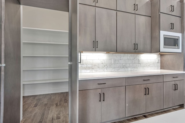 kitchen with stainless steel microwave, dark hardwood / wood-style floors, gray cabinetry, and backsplash