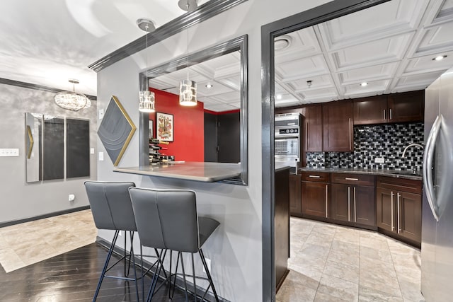 kitchen with coffered ceiling, light hardwood / wood-style flooring, stainless steel fridge, a kitchen bar, and ornamental molding