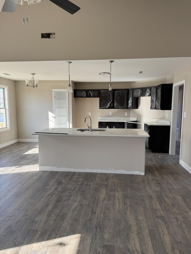 kitchen featuring dark wood-type flooring, sink, hanging light fixtures, a center island with sink, and ceiling fan