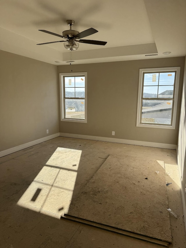 spare room with a raised ceiling, a wealth of natural light, and ceiling fan