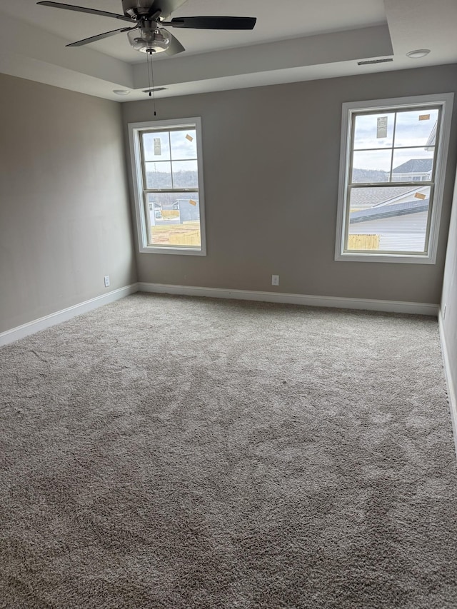 carpeted spare room featuring a tray ceiling and ceiling fan