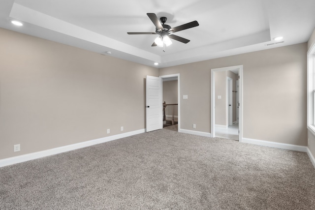 unfurnished bedroom with ceiling fan, a tray ceiling, and carpet