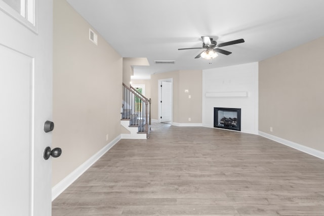 unfurnished living room featuring a fireplace, visible vents, baseboards, stairway, and light wood-type flooring