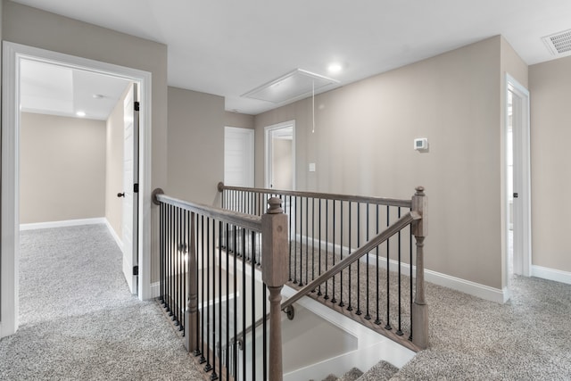 hall featuring attic access, baseboards, carpet flooring, and an upstairs landing