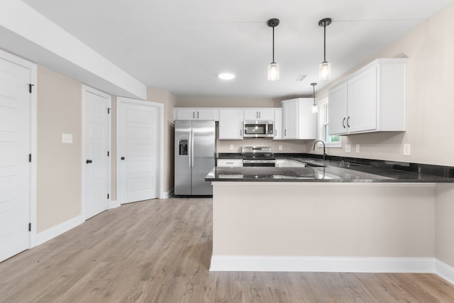 kitchen with stainless steel appliances, decorative light fixtures, light wood-style floors, and a peninsula