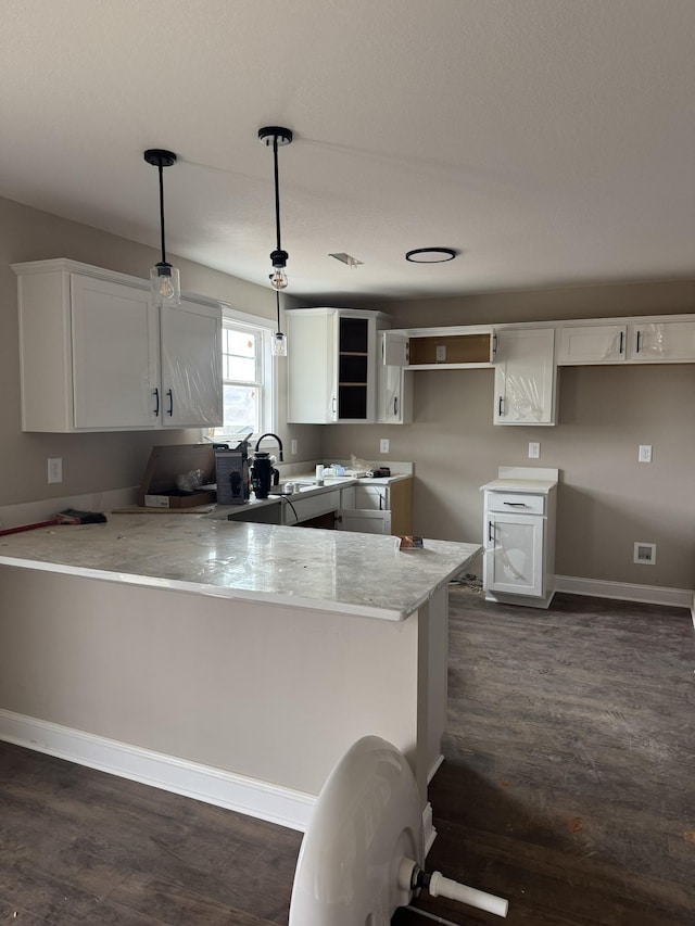 kitchen with a peninsula, light stone counters, white cabinets, and dark wood-style flooring