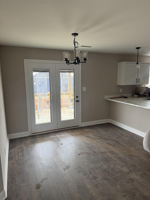 unfurnished dining area featuring an inviting chandelier, baseboards, and dark wood-type flooring