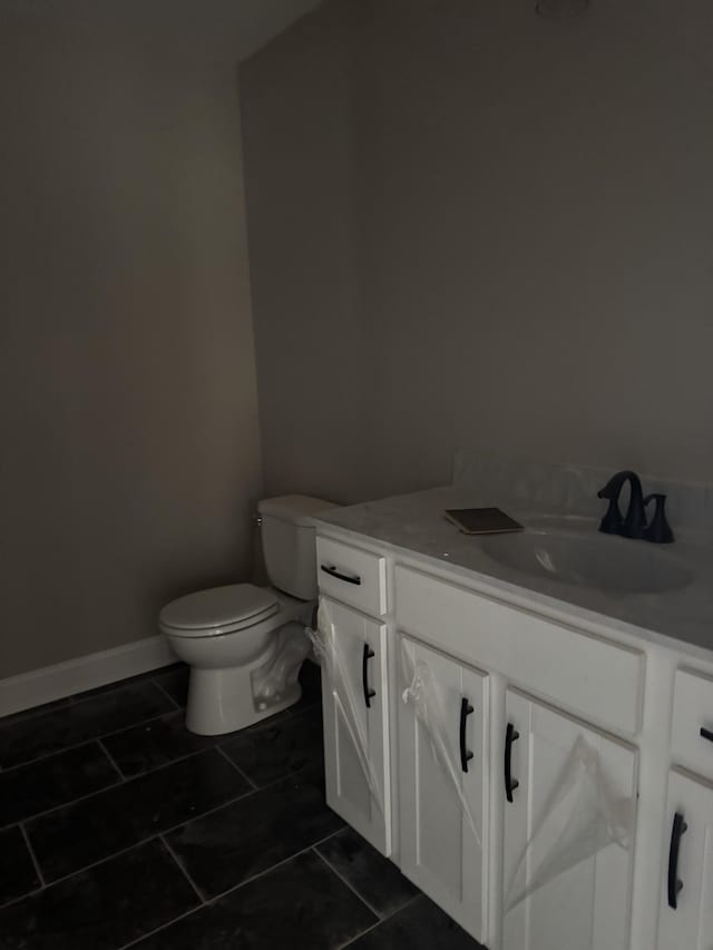 half bath featuring toilet, tile patterned floors, baseboards, and vanity