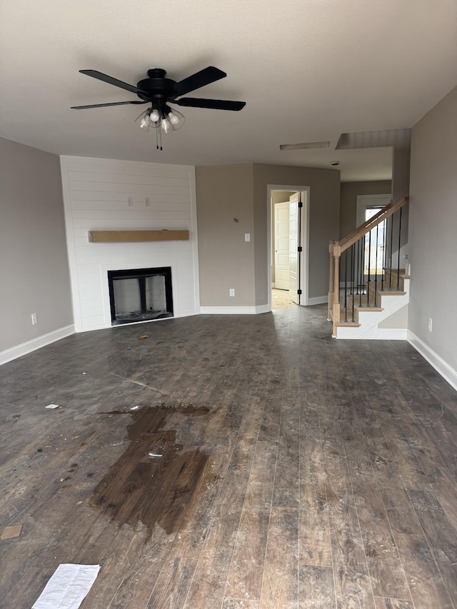 unfurnished living room with a fireplace, wood-type flooring, ceiling fan, baseboards, and stairs