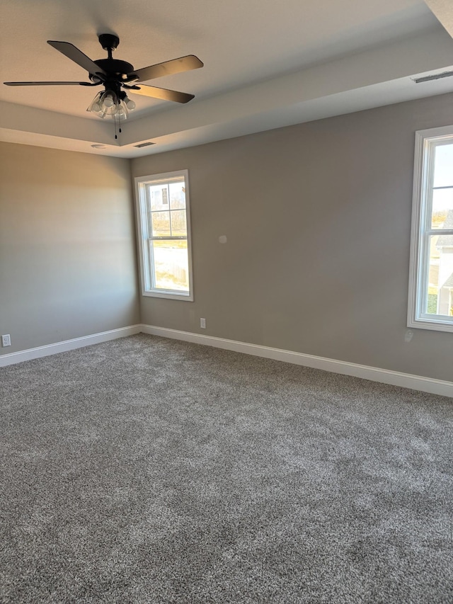 carpeted empty room with ceiling fan, a tray ceiling, plenty of natural light, and baseboards