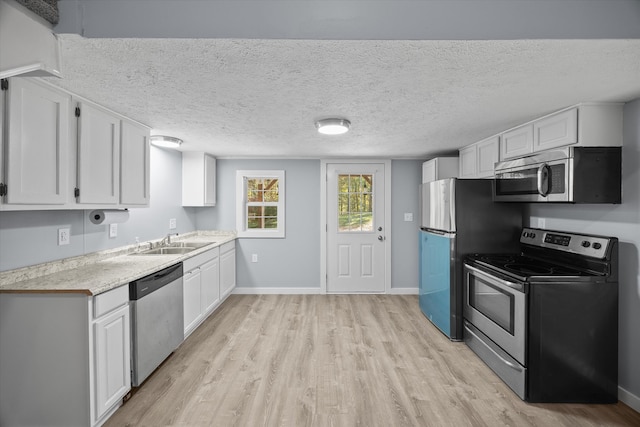 kitchen featuring sink, white cabinets, light wood-type flooring, appliances with stainless steel finishes, and a textured ceiling