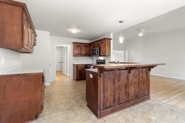 kitchen with kitchen peninsula, appliances with stainless steel finishes, ceiling fan, light hardwood / wood-style floors, and a breakfast bar area