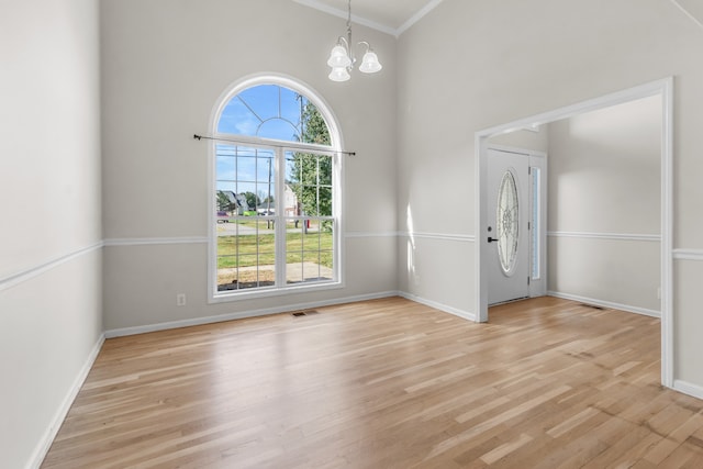 foyer featuring light wood-type flooring, ornamental molding, a towering ceiling, and a chandelier