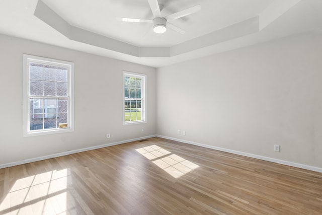 empty room featuring a raised ceiling, ceiling fan, and light wood-type flooring