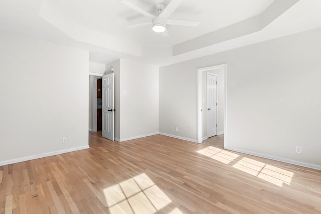 spare room with a raised ceiling, light hardwood / wood-style flooring, and ceiling fan