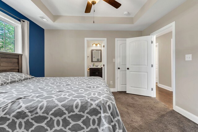 bedroom with ensuite bathroom, dark colored carpet, ceiling fan, and a raised ceiling