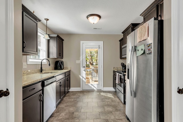 kitchen featuring light stone counters, stainless steel appliances, dark brown cabinets, pendant lighting, and sink