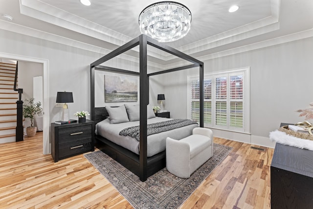 bedroom with a tray ceiling, wood-type flooring, and an inviting chandelier