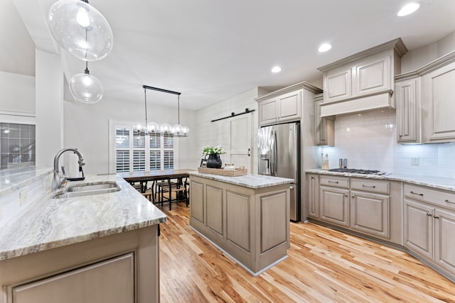 kitchen with a barn door, stainless steel appliances, sink, light hardwood / wood-style floors, and a center island