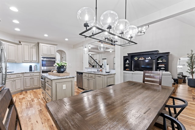 kitchen with appliances with stainless steel finishes, light wood-type flooring, a kitchen island, decorative light fixtures, and light stone counters