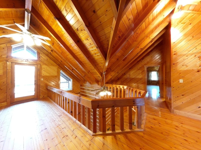 additional living space featuring light hardwood / wood-style floors, wood walls, a healthy amount of sunlight, and vaulted ceiling with beams