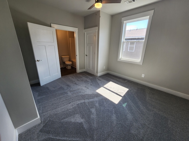 unfurnished bedroom with ceiling fan, ensuite bathroom, and dark colored carpet