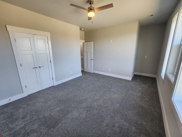 unfurnished bedroom with dark colored carpet, a closet, and ceiling fan