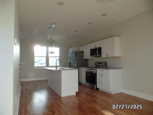 kitchen featuring stainless steel appliances, a sink, white cabinetry, light wood finished floors, and a center island with sink