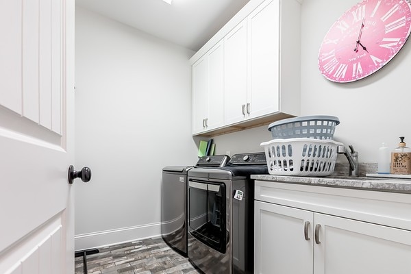 clothes washing area with cabinets, washing machine and dryer, and hardwood / wood-style floors