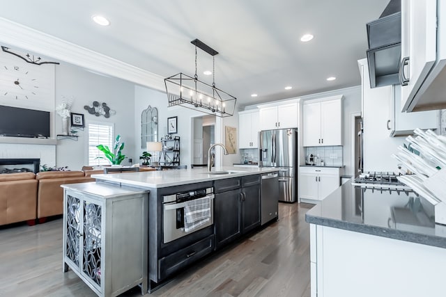 kitchen featuring stainless steel appliances, sink, decorative light fixtures, white cabinets, and an island with sink