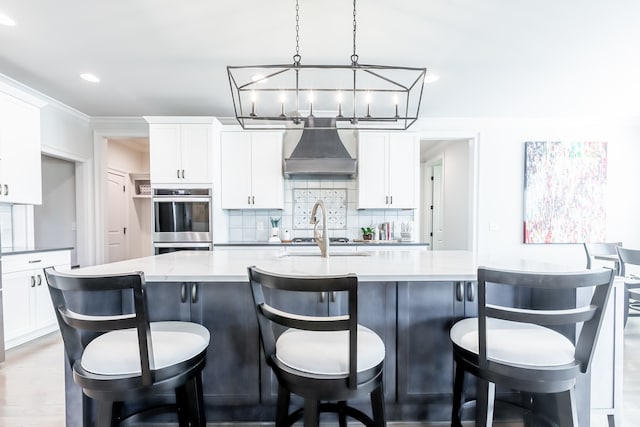 kitchen with wall chimney exhaust hood, light stone countertops, white cabinetry, and a kitchen island with sink