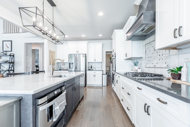 kitchen featuring a spacious island, wall chimney range hood, hardwood / wood-style flooring, appliances with stainless steel finishes, and white cabinetry