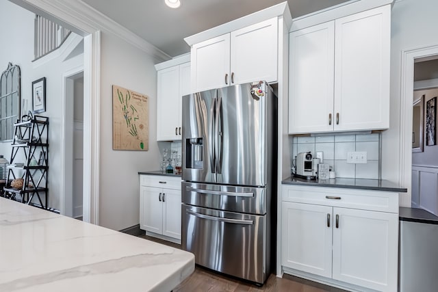 kitchen with white cabinets, stainless steel fridge, decorative backsplash, and dark stone countertops