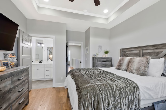 bedroom with ensuite bath, sink, light wood-type flooring, a raised ceiling, and ceiling fan