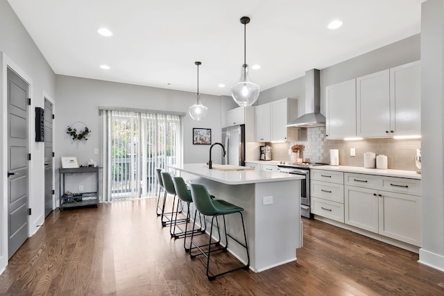 kitchen featuring white cabinetry, wall chimney range hood, appliances with stainless steel finishes, and an island with sink