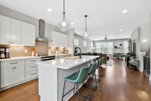 kitchen with a center island with sink, white cabinetry, dark wood-type flooring, wall chimney exhaust hood, and decorative light fixtures