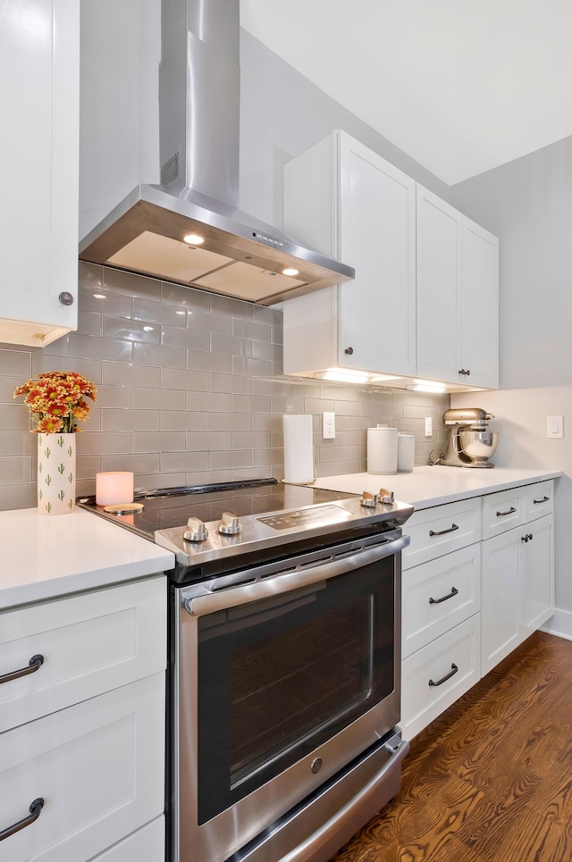 kitchen featuring wall chimney range hood, dark wood-type flooring, backsplash, white cabinets, and stainless steel electric range oven