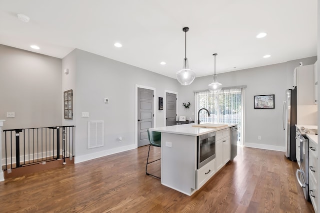 kitchen featuring appliances with stainless steel finishes, hardwood / wood-style floors, decorative light fixtures, white cabinets, and a kitchen island with sink