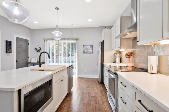 kitchen with wall chimney range hood, dark wood-type flooring, stainless steel appliances, decorative light fixtures, and white cabinetry