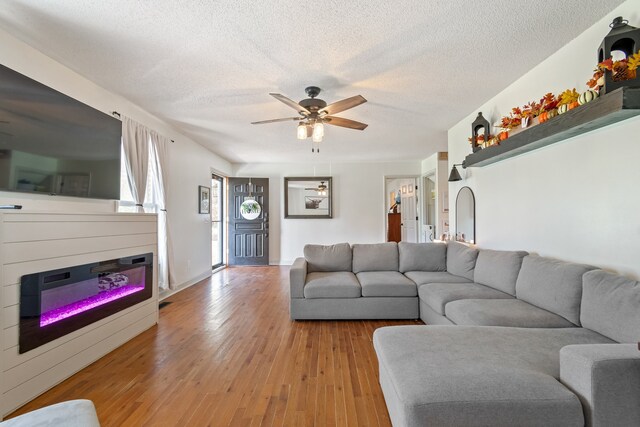 living room with ceiling fan, a textured ceiling, and light wood-type flooring