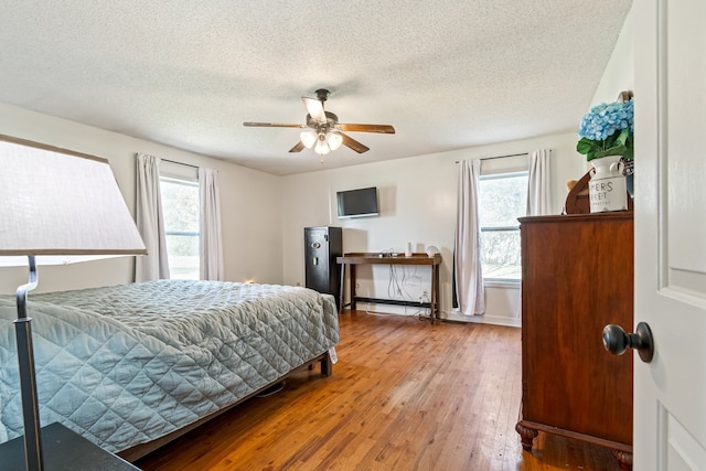 bedroom featuring wood-type flooring, a textured ceiling, multiple windows, and ceiling fan